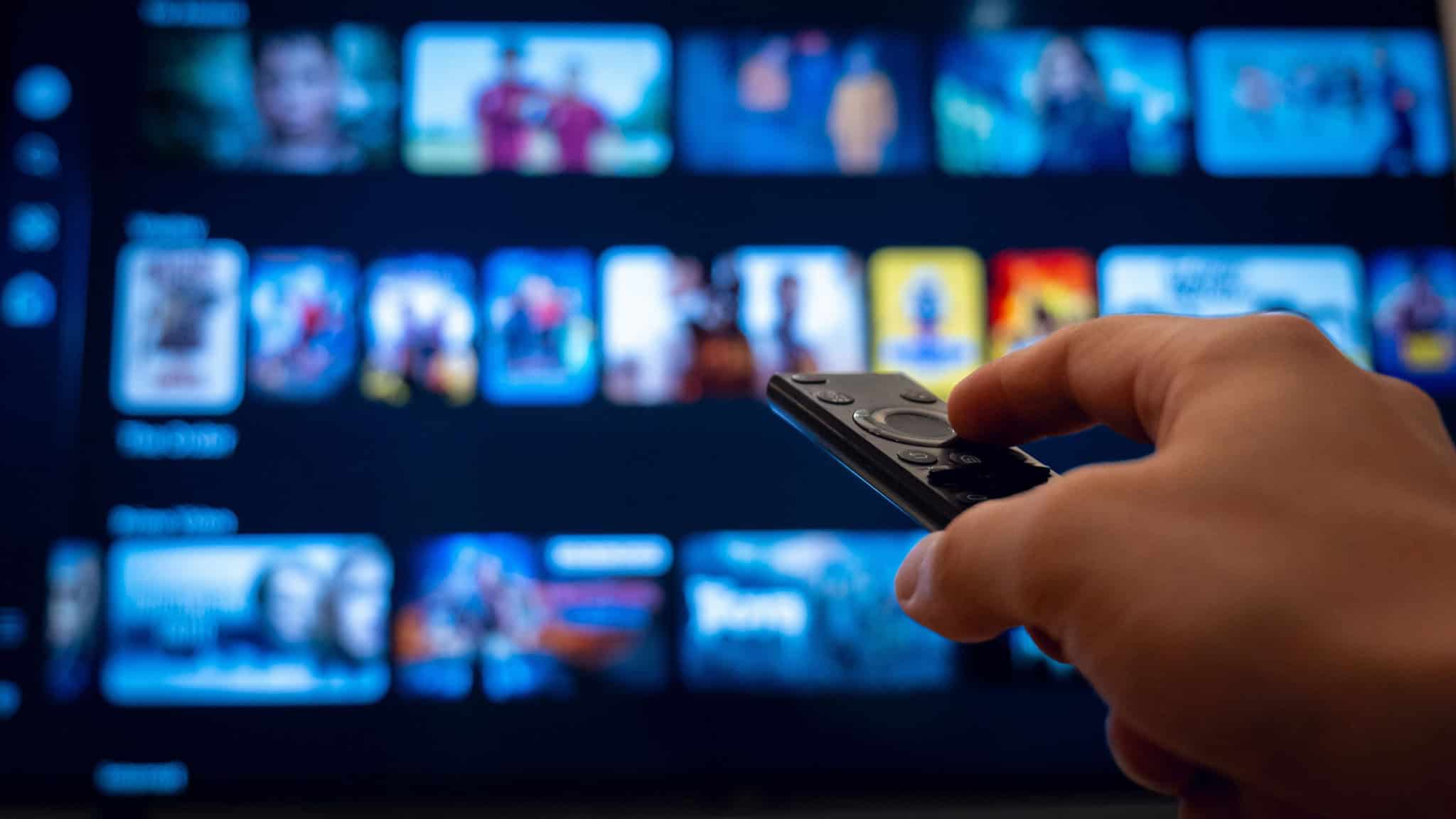 Pessoa segurando controle de smart TV apontando pra ela enquanto escolhe conteúdo em plataforma de streaming