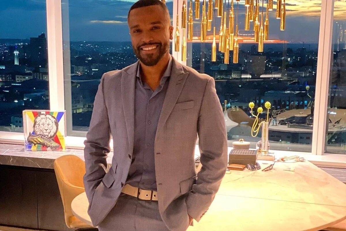 Alexandre Pires posa, sorridente, de terno cinza e as mãos nos bolsos - Metrópoles