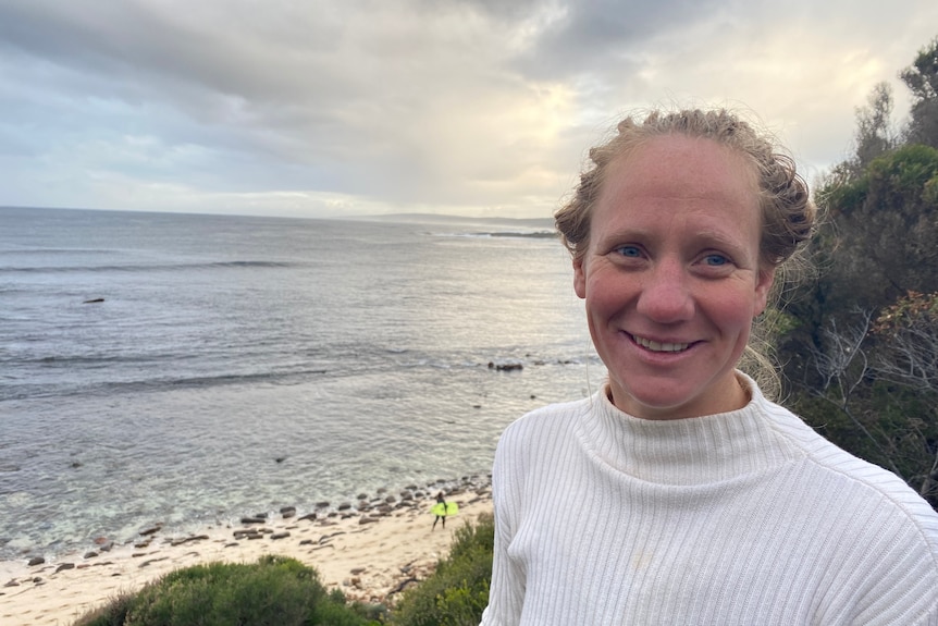 A woman in a white shirt with a beach in the background