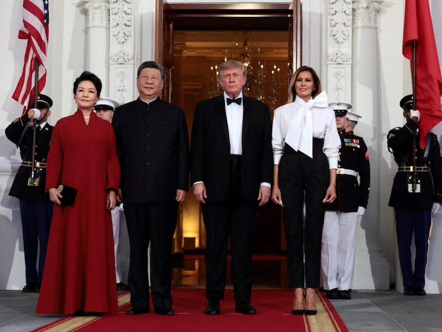 Two couples, men in black suits, one woman in pant suit and another in red gown stand outside White House