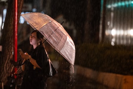 A woman looks at her phone as she walks down the street during a heavy rainstorm in Tokyo.