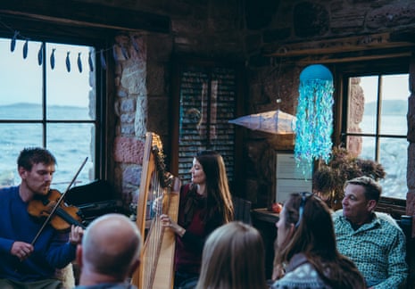 At a herring festival in Achiltibuie, north-west Scotland, a man plays violin as a woman plays harp for seated guests.