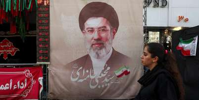 Uma mulher caminha ao lado de um cartaz com a imagem do l&iacute;der supremo do Ir&atilde;, Mojtaba Khamenei, em uma rua de Teer&atilde;, Ir&atilde;, em 13 de agosto de 2026. Foto: via REUTERS - Majid Asgaripour / RFI