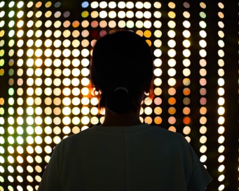 Rear view, silhouette of a young woman standing against illuminated LED digital display screen in the dark