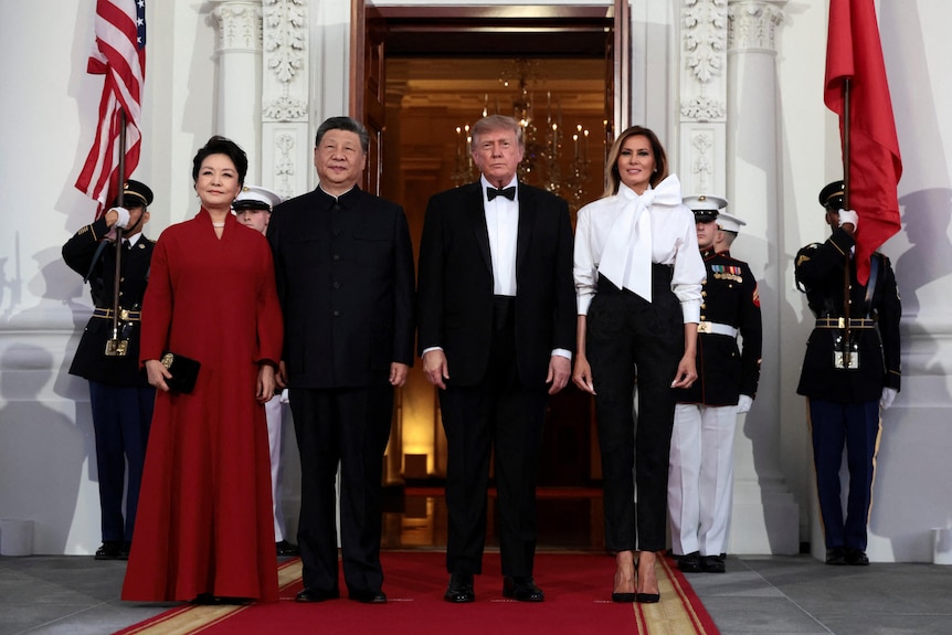 two couples, men in black suits, one woman in pant suit and another in red gown stand outside White House