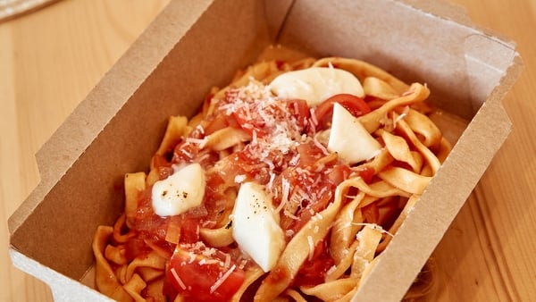 Eco-friendly box containing pasta topped with fresh tomatoes and mozzarella