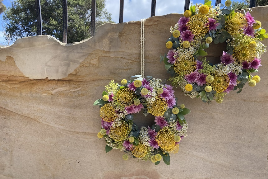 Two pink and yekllow fresh flower wreaths hanging on a piece of wood.