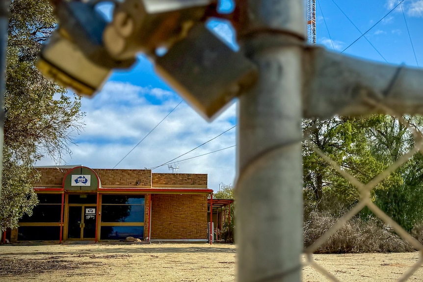 A padlocked gate in front of a dirt road and a building, with a sign reading WIN Television.