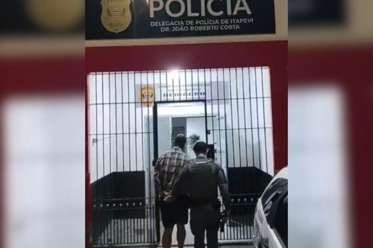 Foto colorida de homem sendo conduzido para delegacia por policial militar.