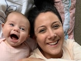 A baby smiling laying next to a woman who is also smiling